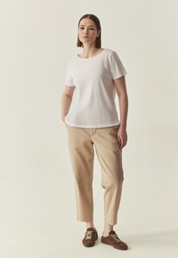T-shirt blanc à manches courtes associé à un pantalon beige clair et des chaussures marron à lacets, présentant une coupe décontractée et une texture de tissu lisse.