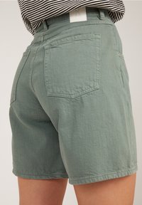 Green cotton shorts featuring a relaxed fit, five pockets, and a cuffed hem. Textured fabric with a soft finish.