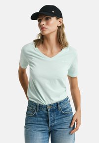 Mintgrøn, kortærmet V-hals t-shirt lavet af blødt stof, parret med blå højtaljede denim jeans. Sort kasket med gyldne detaljer synlig.