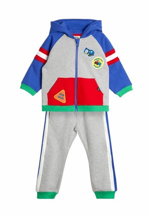 Hoodie-Trainingsanzug in Blau, Grau und Rot. Verfügt über bunte Patches, einen Reißverschluss und gerippte Manschetten. Graue Hose mit blauen und weißen Streifen.