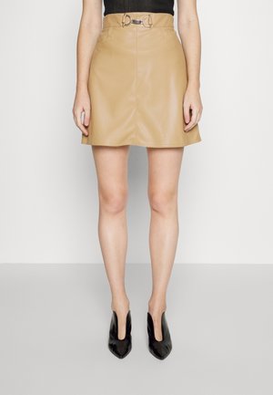 Jupe mini en simili cuir beige avec une taille ajustée, dotée d'une boucle circulaire en acier inoxydable. Texture lisse et silhouette évasée.