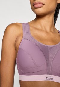 Αθλητικό σουτιέν λεβάντας με δομημένο σχέδιο, ρυθμιζόμενους ιμάντες και ροζ ταινία. Σημαντικές λεπτομέρειες ραφής ενισχύουν τη συνολική εφαρμογή και υποστήριξη.