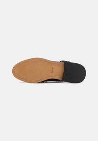 Black woven upper shoe with a beige sole, featuring stitching details and a smooth finish. Sole has textured grip areas.