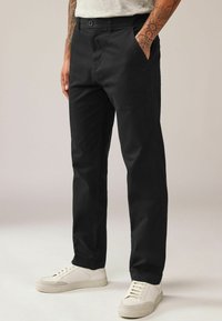 Pantaloni negri din material durabil, cu croi drept, buzunare laterale și închidere cu nasturi, asortați cu adidași albi.