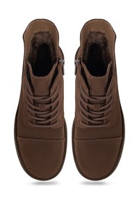 Botas de tobillo de ante marrón con un interior suave, punta redonda, cordones en la parte delantera y cremallera lateral. Suela plana de goma con un diseño minimalista.