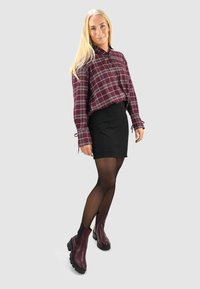 Bordeaux geruite blouse met knoopdetails, zwarte minirok, doorzichtige zwarte panty's en bordeaux enkellaarsjes met dikke zolen.