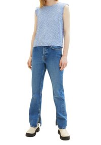 Jasnoniebieski top bez rękawów z kropkowanym wzorem, w połączeniu z wysokim stanem niebieskich dżinsów z bocznymi rozcięciami przy nogawkach oraz czarnymi butami.
