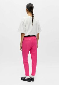 Pantalon rose fuselé avec une ceinture élastique et deux poches arrière. Assorti à un t-shirt blanc ample et des chaussures noires.