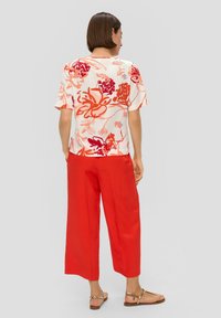 Bloes met bloemenprint en korte mouwen in wit, rood en roze; gecombineerd met losse, felrode linnenbroek en platte gouden sandalen.