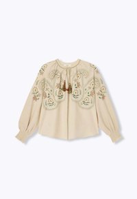 Blouse beige avec broderies florales, dotée d'un col rond, de manches froncées et d'accents en pompons au niveau de la fermeture à nouer. Textile doux.