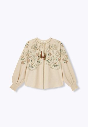 Blouse beige avec broderies florales, dotée d'un col rond, de manches froncées et d'accents en pompons au niveau de la fermeture à nouer. Textile doux.