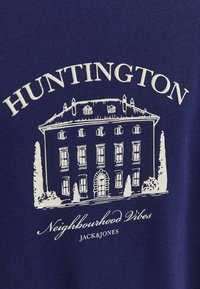 T-shirt bleu marine avec un graphique blanc d'un bâtiment avec "HUNTINGTON" au-dessus et "Neighbourhood Vibes JACK&JONES" en dessous, avec des lignes architecturales détaillées.