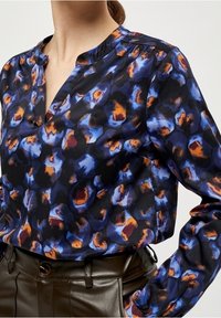 Långärmad blus med v-ringning, med ett blått, orange och svart leopardmönster på ett lätt, texturerat tyg.