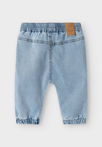 Pantaloni di denim azzurro chiaro con cintura elastica, caviglie arricciate e un'etichetta marrone sul retro. Caratterizzati da dettagli di cucitura classici.