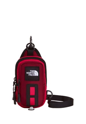 Kompaktowa czerwona i czarna saszetka North Face z kieszeniami na zamek, regulowanym czarnym paskiem i naszywką z logo marki z przodu.