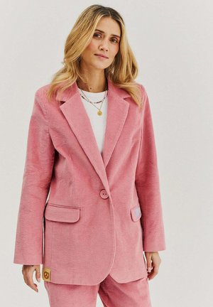 Růžový kordový blazer s výstřihy, dvěma předními kapsami a zapínáním na jedno knoflíkové. Obsahuje malou akcentovou nášivku na boku.