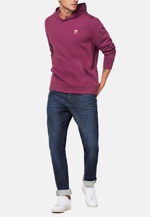 Bordeauxfarbene Kapuzenpullover mit Kängurutasche, gerippten Bündchen und Saum. Kombination mit dunkelblauen Jeans und weißen Sneakern. Lässiges, bequemes Outfit.