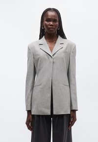 Γκρι σακάκι με εφαρμοστή γραμμή, γιακάδ�ες με σχισμές, κλείσιμο με ένα κουμπί και ελαφριά επένδυση στους ώμους. Διαθέτει τσέπη στο στήθος και πλαϊνές τσέπες.