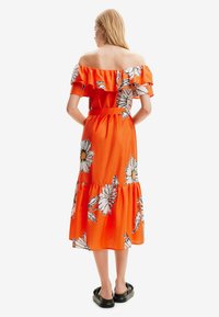 Off-shoulder oranje jurk met een bloemenpatroon, gerimpelde mouwen en een gelaagde zoom. Gekocht met zwarte platte sandalen. Glad materiaal.