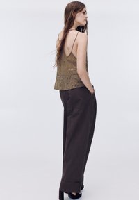 Világosbarna gyöngyökkel díszített ujjatlan felső bonyolult mintákkal, laza, sötétbarna nadrággal, magas derékkal és oldalzsebekkel.