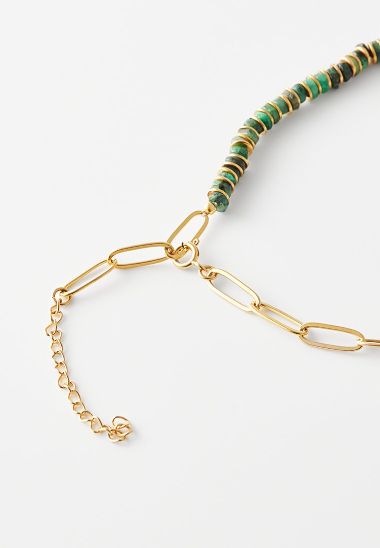 Collier en chaîne dorée avec des maillons rectangulaires et une section de perles en pierres vertes et noires, fermoir en argent sur fond blanc.