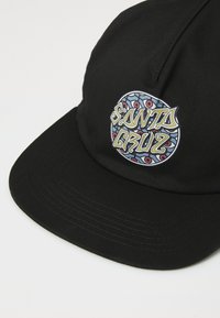 Black cap featuring a colorful circular "Santa Cruz" patch with intricate designs and lettering on the front. Stitched visor and textured fabric.