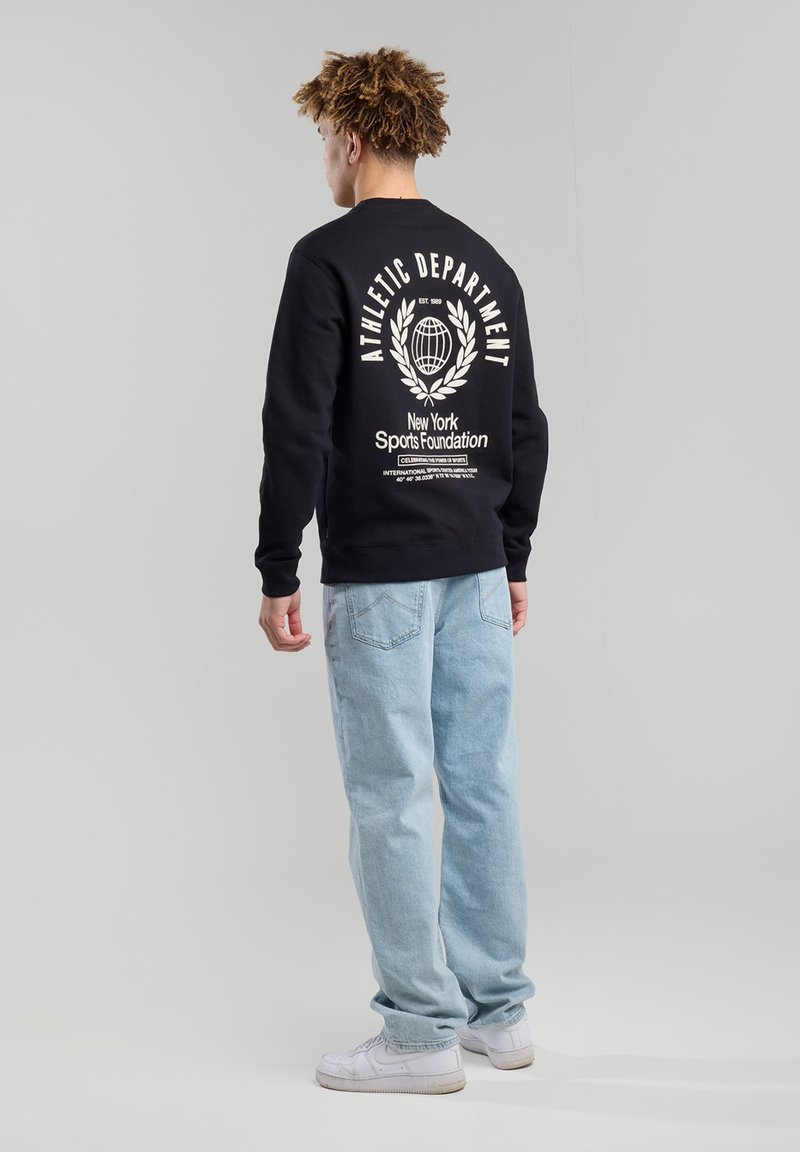 Black sweatshirt with "ATHLETIC DEPARTMENT" text, crew neck, and graphic print on back; paired with light blue jeans and white sneakers.