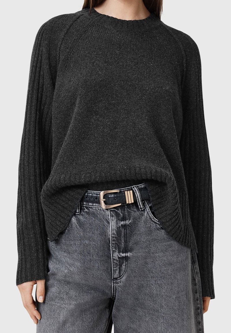 Femme portant un pull en maille côtelée gris foncé rentré dans un jean noir délavé taille haute avec une ceinture noire et une boucle rectangulaire dorée.