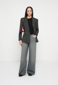 Kétsoros szürke tűzött csíkos blézer, fekete felső, bőszárú világos farmernadrág, fekete cipő és egy kis bordó kézitáska.