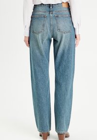 Lysblå, højtaljede denimjeans med en afslappet pasform, der har baglommer og et lædermærke på taljen, vist fra ryggen.