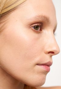 Profile view of a face with fair skin, straight nose, and subtle lip color. Notable smooth texture and greenish-brown eye.