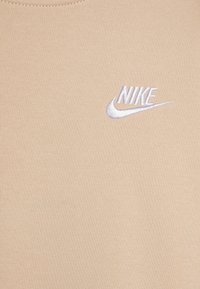 Bežs kokvilnas t-krekls ar apaļu kakla izgriezumu. Uz kreisās krūts puses ir iešūta balta Nike logo. Mīksta tekstūra.