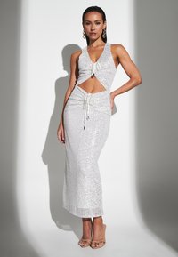 Silver sequined dress with a deep V-neck and cut-out sides, featuring drawstring details. Model wearing nude high-heeled shoes.