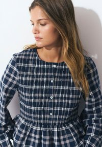 Navy and gray checkered dress with smocked bodice, long sleeves, round neckline, and button closures. Soft cotton fabric, flared skirt.