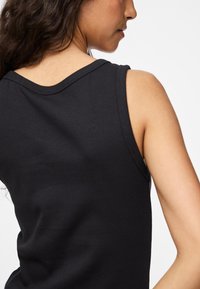 Černý žebrovaný top bez rukávů s širokými průramky a kulatým výstřihem, který zobrazuje hladkou texturu bez viditelných švů nebo vzorů.