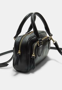 Sac à main en cuir noir avec deux zips dorés, poignées courtes et une bandoulière amovible. Forme rectangulaire avec une texture lisse et un design minimaliste.