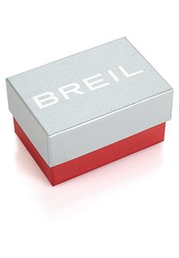 Silverfärgad fyrkantig box med röd botten, med varumärket "BREIL" i fetvita bokstäver på locket. Slät yta.