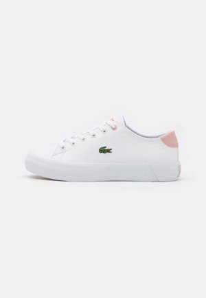 Hvit sneaker med en teksturert gummisåle, rosa hæltab og grønn krokodillelogo. Kjennetegnes ved klassisk snøring med sømde detaljer.
