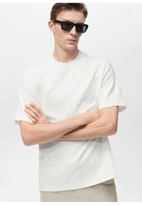 Tricou alb cu mânecă scurtă, cu decolteu rotund, realizat dintr-un material moale. Modelul poartă ochelari de soare rectangulari negri, cu brațele încrucișate.
