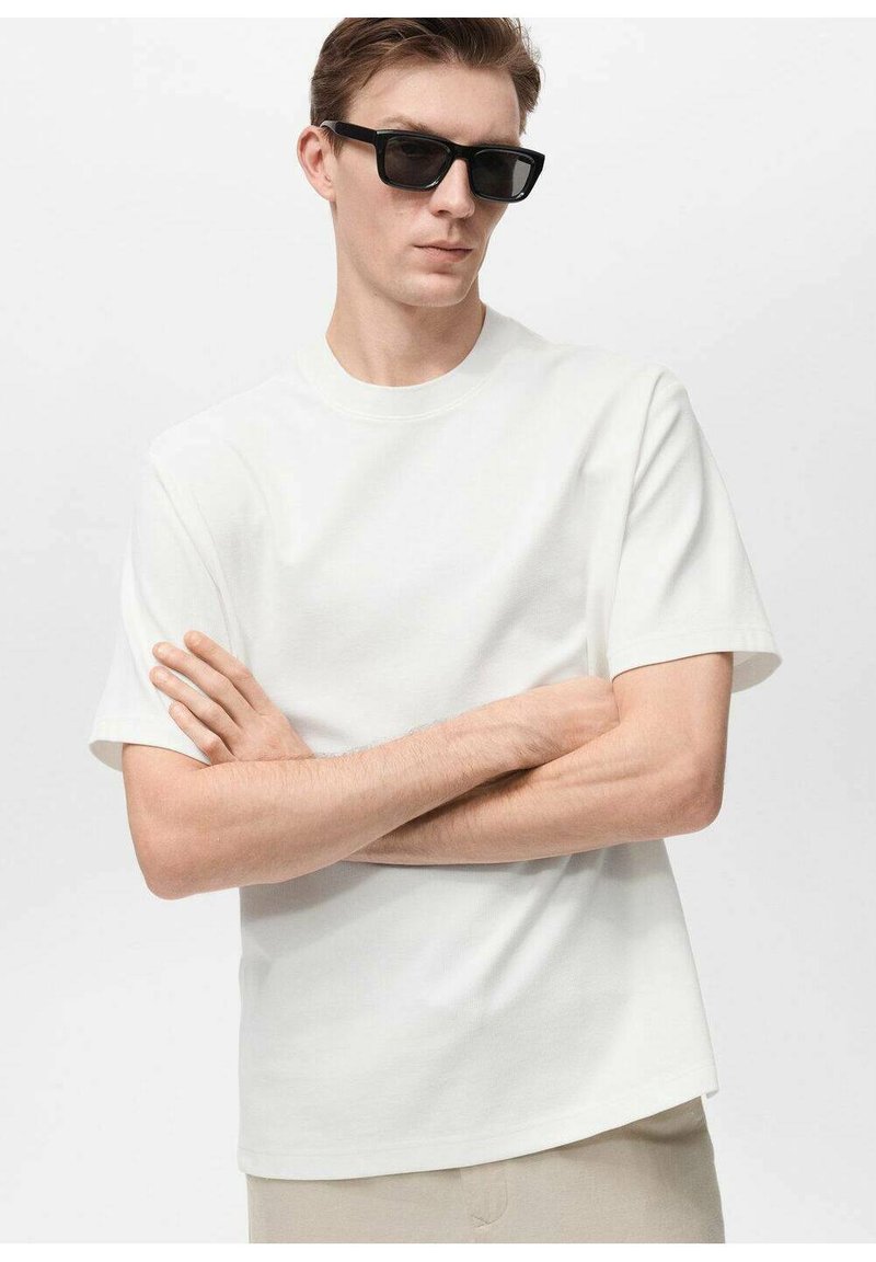 Tricou alb cu mânecă scurtă, cu decolteu rotund, realizat dintr-un material moale. Modelul poartă ochelari de soare rectangulari negri, cu brațele încrucișate.