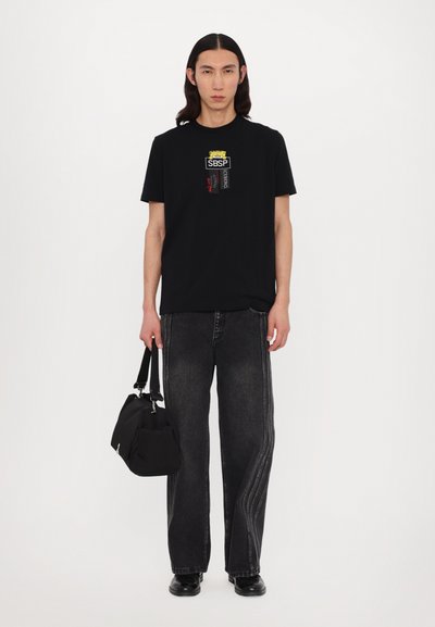 Sort t-shirt med grafisk print, parret med sort lige ben jeans med sidelæg, og en sort håndtaske med korte håndtag.