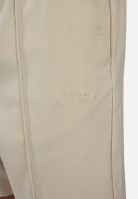 Beige shorts lavet af tekstureret stof med en sidelomme. Har et broderet "PEGADGR" logo i en diskret farve på venstre ben.