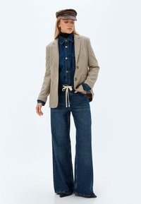 Ruudullinen vaaleanbeige bleiseri sinisen denim-paidan päällä, yhdistettynä leveälahkeisiin sinisiin farkkuihin ja ruskeaan lippalakkiin. Kangasrakenteet vaihtelevat.