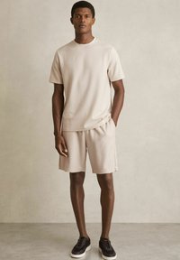 Beige ribbet t-shirt med korte ærmer og matchende shorts, med en afslappet pasform. Sættet er parret med sorte sneakers med et struktureret design.
