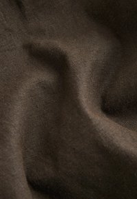 Mörkbrun tyg med en texturerad, lätt rynkad yta, gjord av ett naturfiber, som visar subtila variationer i ton.