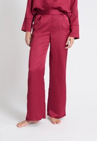 Bordeaux satijnen pyjamabroek met een gladde textuur, wijde pijpen en een subtiel stippenpatroon. Voorzien van een elastische tailleband en zijzakken.