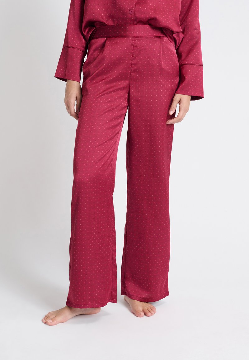 Bordeaux satijnen pyjamabroek met een gladde textuur, wijde pijpen en een subtiel stippenpatroon. Voorzien van een elastische tailleband en zijzakken.