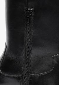 Botas de cuero negras hasta la rodilla con cremallera lateral y detalles en costura, con una textura suave y un diseño de panel curvado.