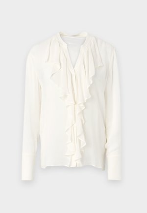 White blouse with long sleeves and a ruffled front placket, featuring a round neckline and button closure. Soft, lightweight fabric.
