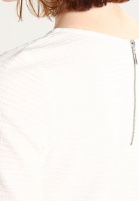 White textured top with a ribbed design and a back zipper closure. The fabric appears soft with a slightly raised pattern.